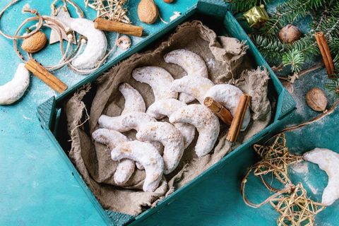 Homemade Christmas nuts cookies crescent with sugar powder in wooden boox with holiday star decoration and fir tree over turquoise wood texture surface with copy space. Top view.