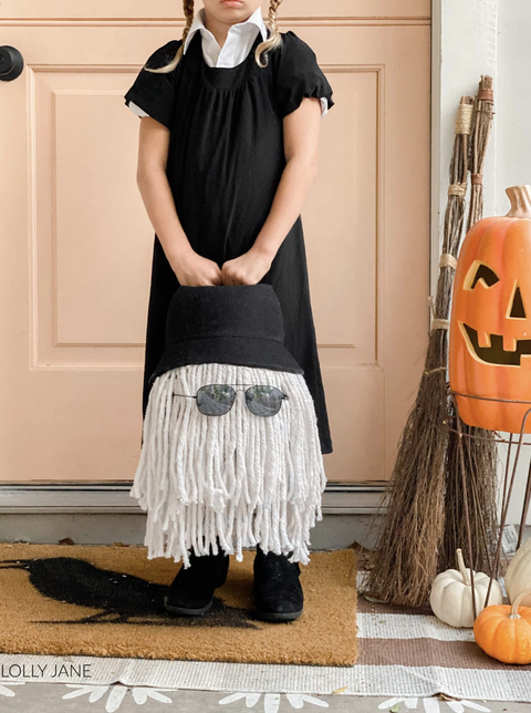 homemade halloween costumes wednesday and it, girl dressed in black dress while holding a bucket with sunglasses, string of white yarn and a black hat