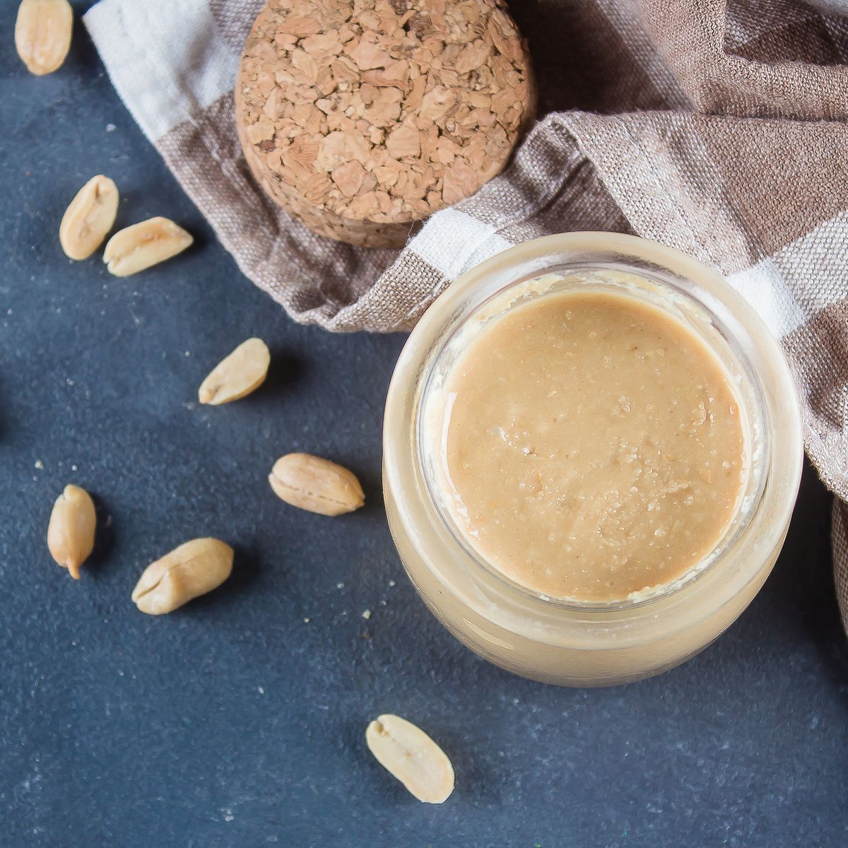 Homemade Peanut butter in glass jar and peanuts on blue concrete table background. Top view