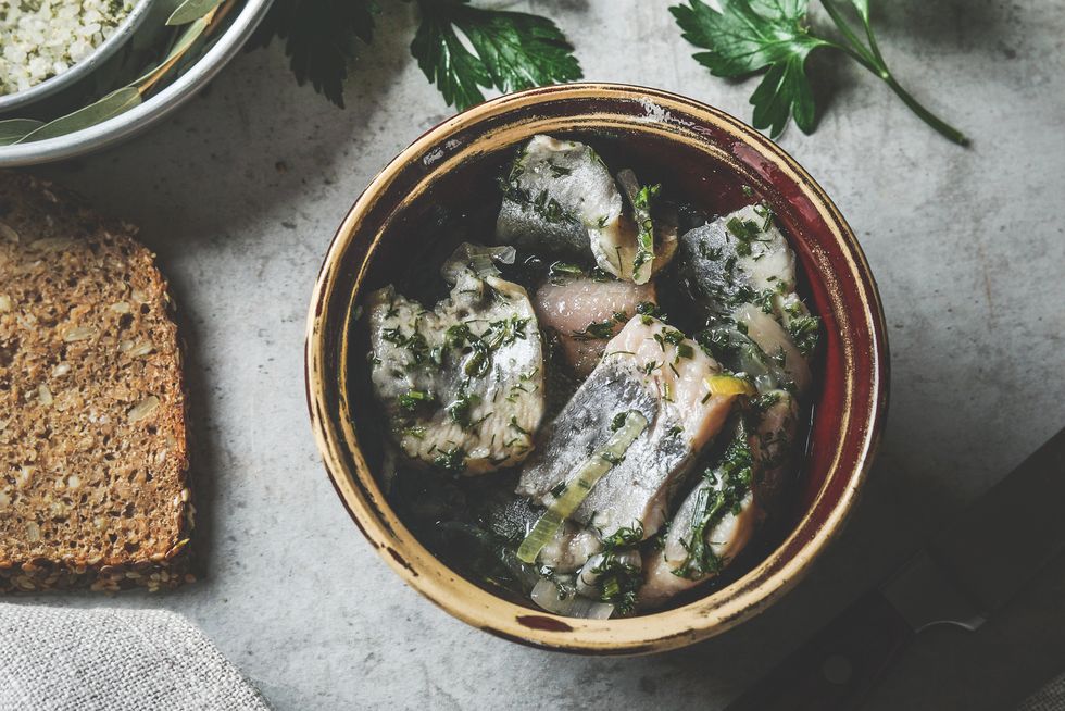 homemade pickled herring with parsley and bread at kitchen table with grey table cloth