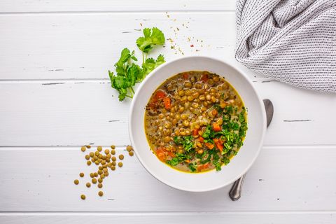 Homemade vegan lentil soup with vegetables and cilantro, white wooden background.