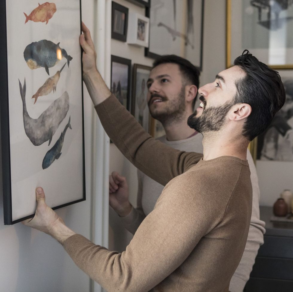 homosexual couple hanging painting on wall at home