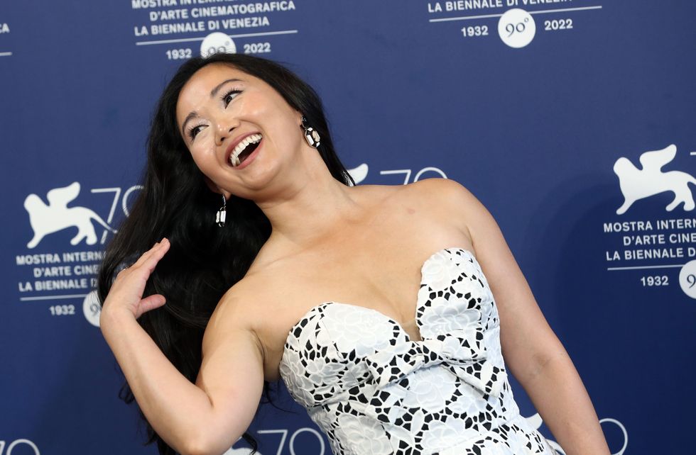 hong chau smiling and tossing her hair back with her right hand, wearing a blue dress and standing in front of a blue photoshoot backdrop