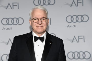 steve martin smiles at the camera, he wears glasses and a black tuxedo