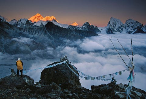 Te midden van gebedsvlaggen op de top van de Gokyo Ri in Khumbu Nepal bekijkt een bergbeklimmer hoe de zon de top van de Mount Everest goud kleurt