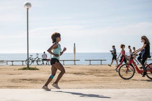 una mujer corre por un paseo marítimo de españa y se cruza con alguien que sale en bicicleta respetando los horarios establecidos para salir a hacer deporte en la fase 2 del confinamiento