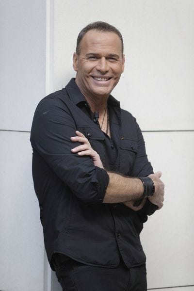 el presentador carlos lozano posando sonriente con los brazos cruzados