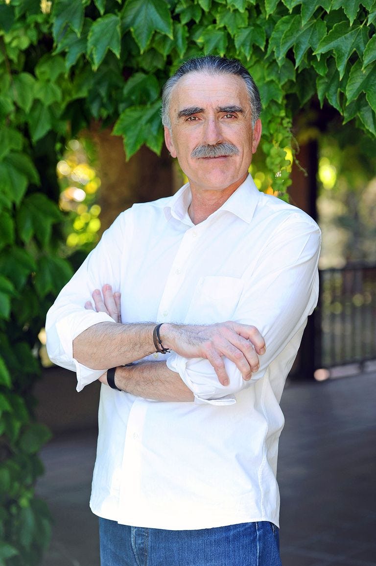 el presentador juan y medio posando de pie con los brazos cruzados