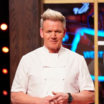 gordon ramsay stands in his chef jacket and looks at the camera, he hands are clasped in front of him