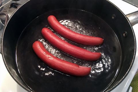 simmering 3 hot dogs in water on stove
