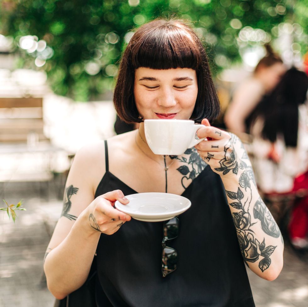 woman sitting in a cafe in the sunshine drinking out of a tea cup