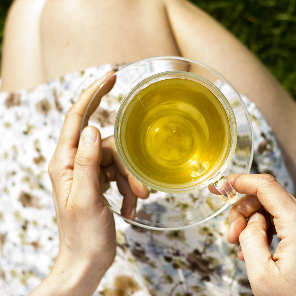 woman resting cup of herbal tea on her legs while sitting on the grass