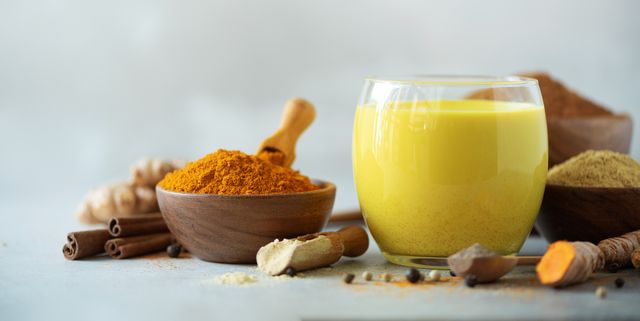 Hot healthy drink. Turmeric latte, golden milk with turmeric root, ginger powder, black pepper over grey background. Copy space. Spices for ayurvedic treatment. Alternative medicine concept.