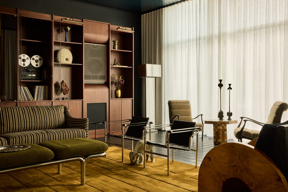 custom brown shelving features a sound system the room has a striped sofa a golden rug and a collection of midcentury furniture
