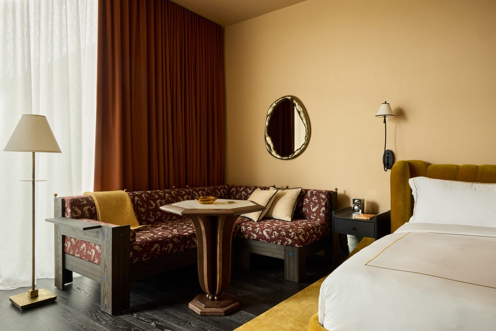 yellow hotel bedroom with velvet mustard colored bed and a corner sofa with a heptagonal table