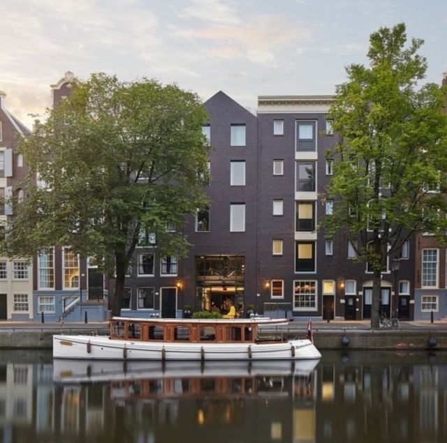 pulitzer amsterdam facade with trees and a boat in the water