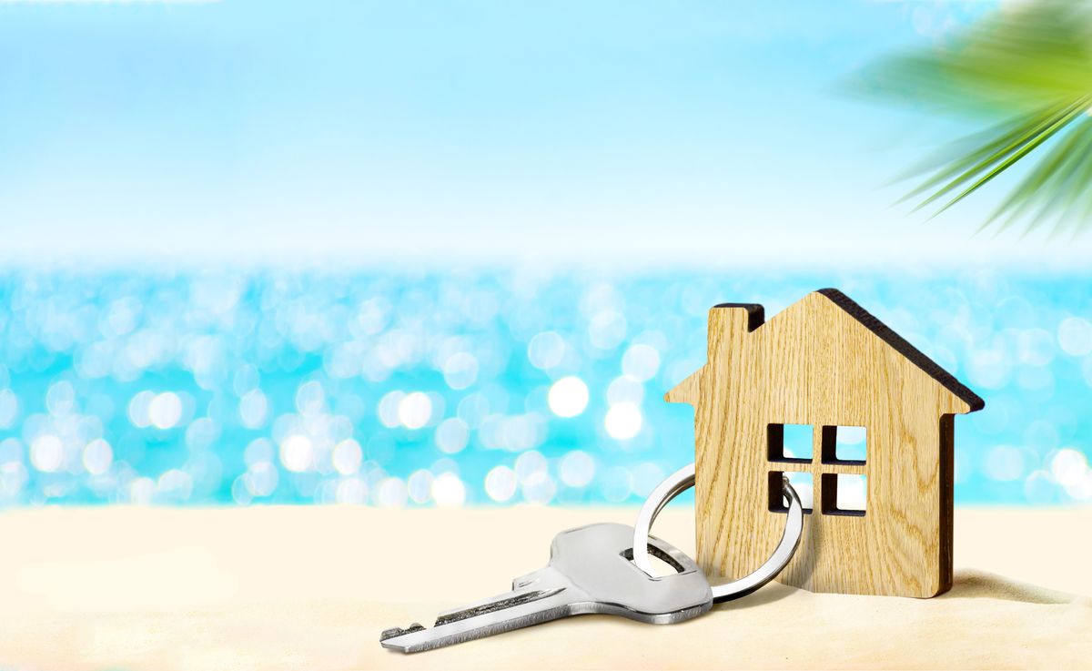 house by the sea concept figure of house and key on sandy beach