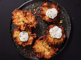 latkes topped with sour cream and chives on a black plate