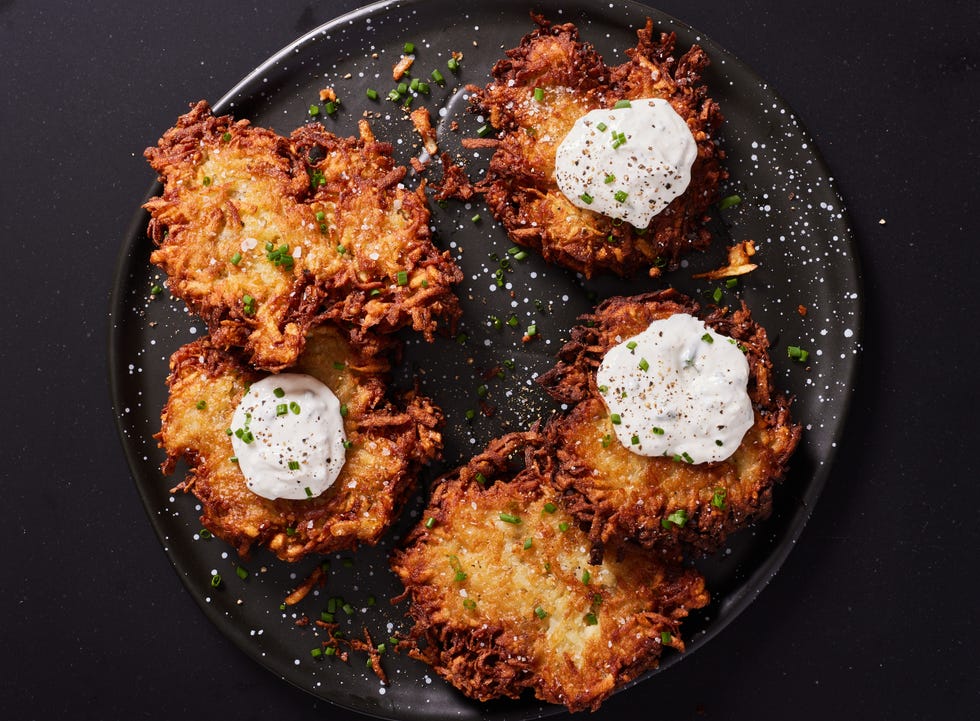latkes topped with sour cream and chives on a black plate
