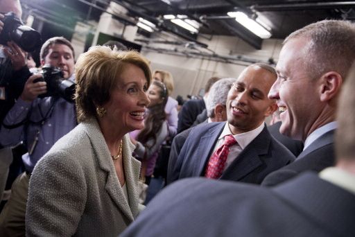 nancy pelosi, hakeem jeffries, and sean patrick maloney smile as they look among one another, they are surrounded by a crowd of people, including photographers