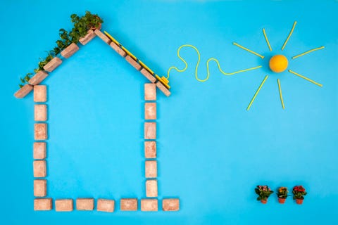 house shape made of bricks on blue background, with solar panels plugged to sun