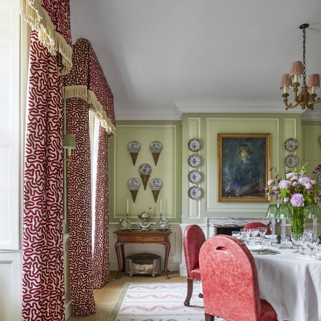 a vibrant varied mix of reds in distressed leather chairs and a painterly rug and velvet on silk draperies animates the dining room