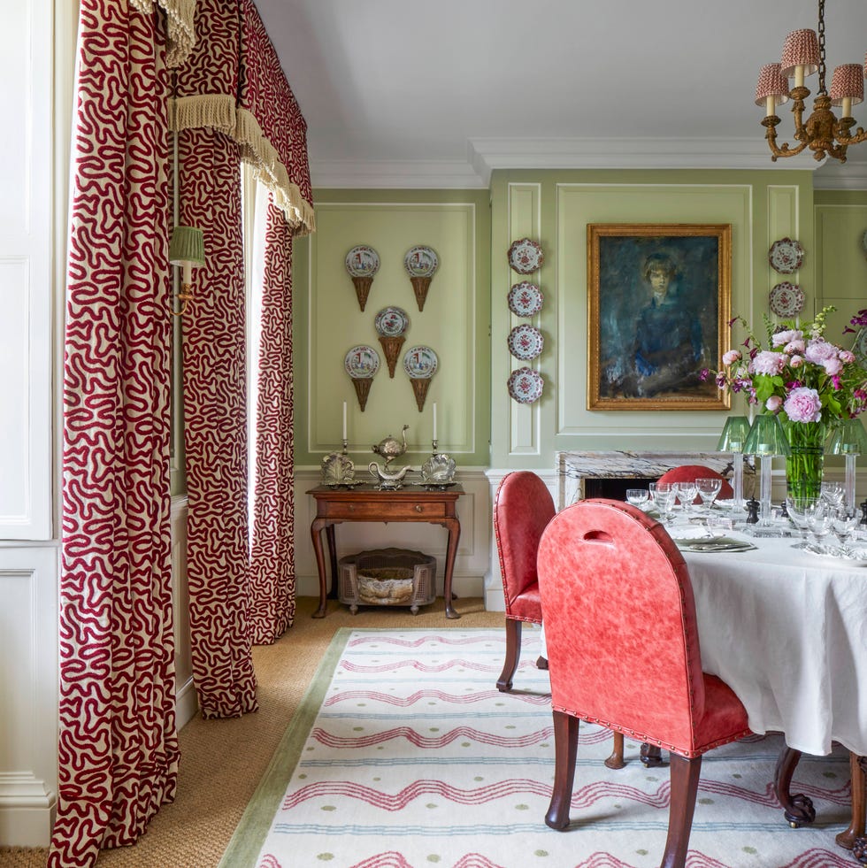 a vibrant varied mix of reds in distressed leather chairs and a painterly rug and velvet on silk draperies animates the dining room