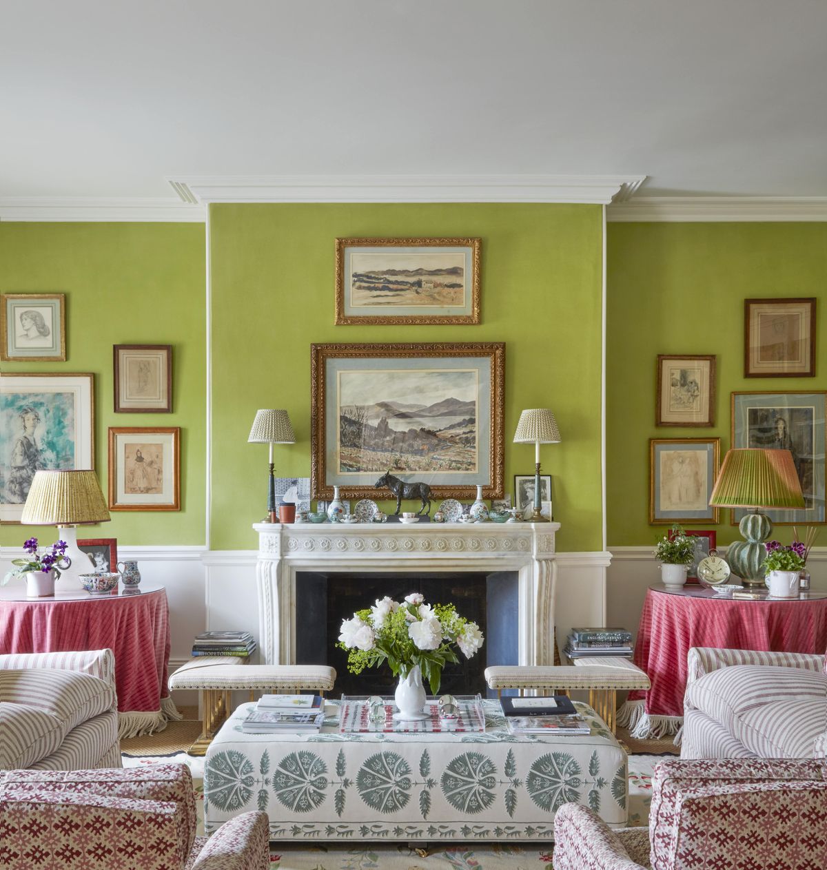 landscape paintings hang above the fireplace in a sitting room with green walls