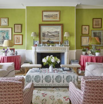 landscape paintings hang above the fireplace in a sitting room with green walls