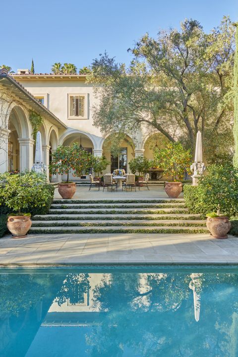 an olive tree shades the pool terrace furnished with a stone table and wrought iron chairs
