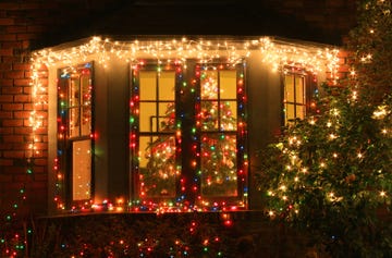 house decorated with christmas lights with a christmas tree visible through the window