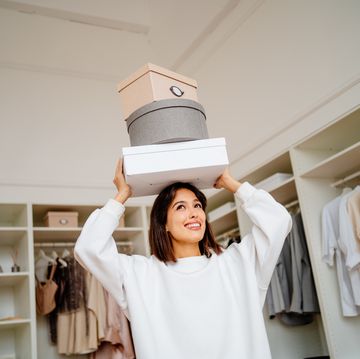 housekeeping and moving clothes boxes. smiling woman carrying clothes boxes on her head near walk in wardrobe