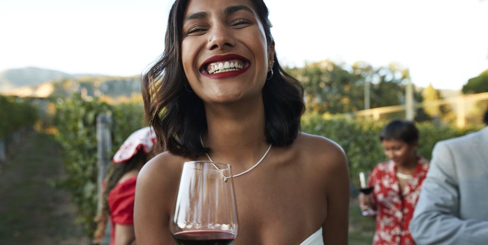 happy young woman wearing bridal gown holds glass of red wine as she dances at party