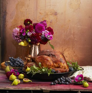 a golden thanksgiving turkey on the dinner table served on a platter with fresh fruit