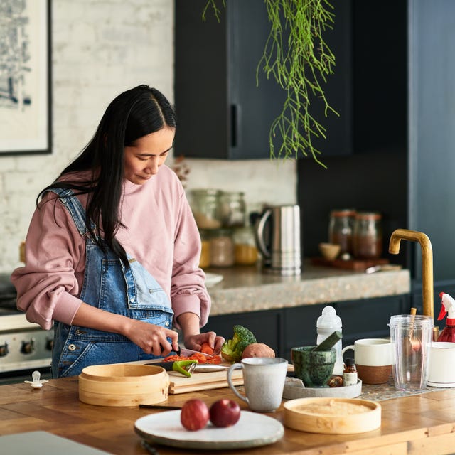 how many calories should a woman eat, mid adult woman chopping ingredients for meal, standing behind kitchen worktop, concentration, precision, cutting