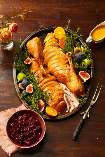 sliced thanksgiving turkey on a platter with figs, herbs and other fruits