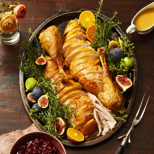 sliced thanksgiving turkey on a platter with figs, herbs and other fruits