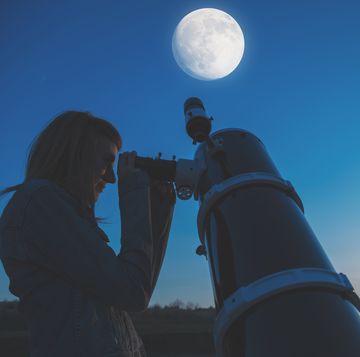 girl looking at a full moon through a telescope