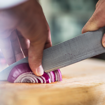slicing a red onion on wooden cutting board