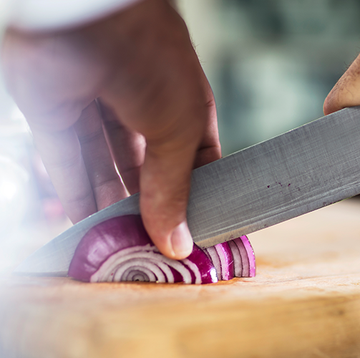 slicing a red onion on wooden cutting board