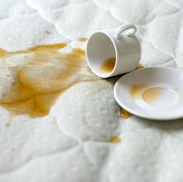 spilled cup of tea on the bed accidentally dropped cup with saucer on white bedsheet unlucky, unfortunate breakfast wet spot