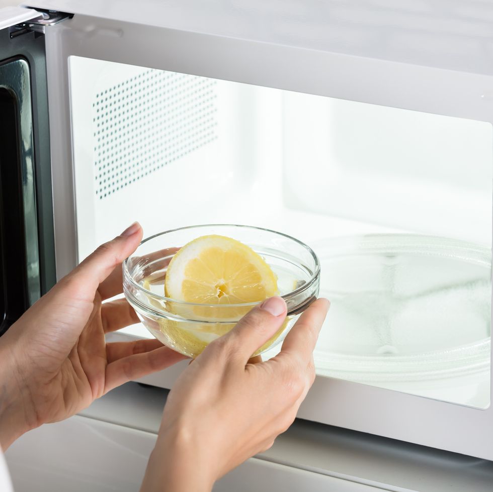 how to clean a microwave, close up of woman putting a bowl of sliced lemon in a microwave oven