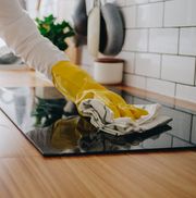 young woman cleaning up the perfect surface of black ceramic kitchen stove and counter using gloves and mop