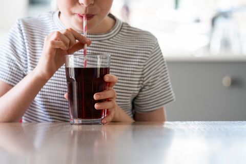 a young child uses a paper straw to drink soda, a beverage that can also be used to clean an electric kettle
