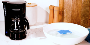coffee maker on marble countertop next to a bowl of soapy water with a sponge