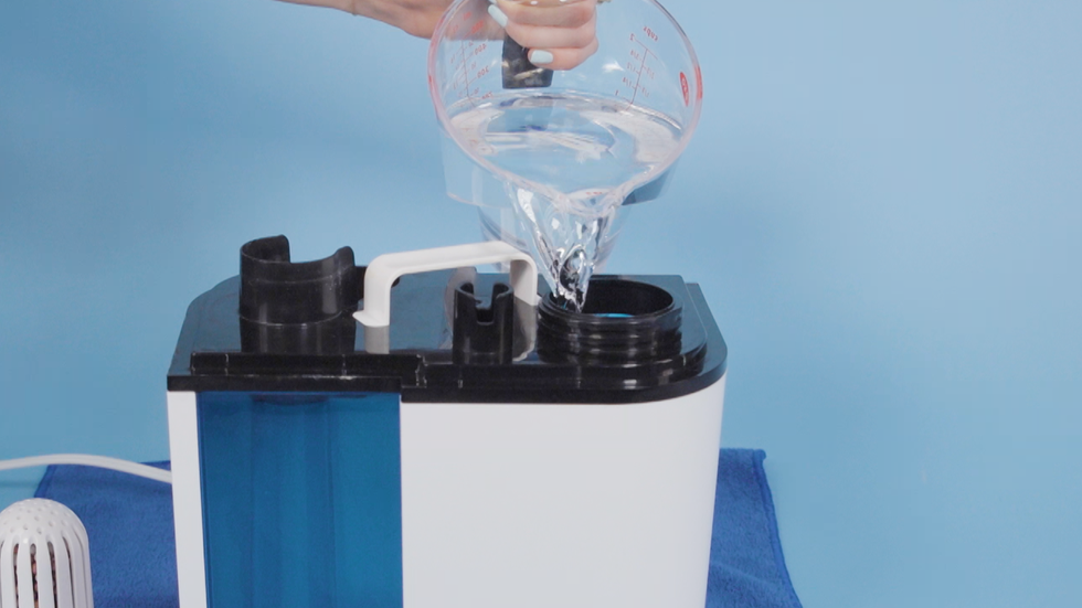 how to clean humidifier, hand pouring white vinegar inside the humidifier from the top