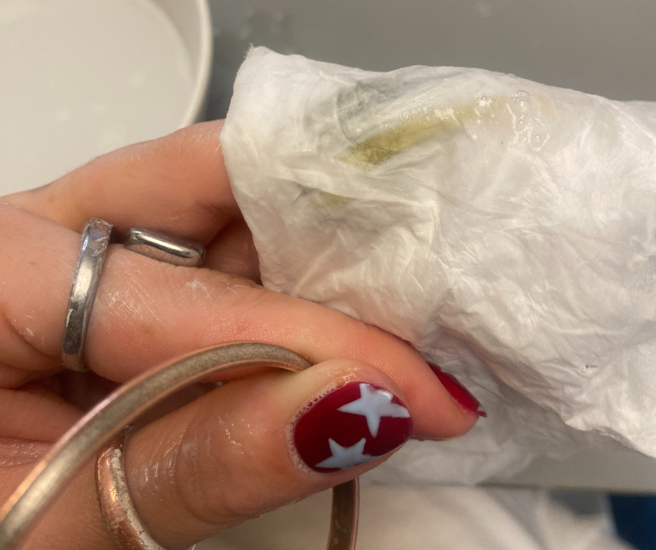 hand holding a tissue with a small object possibly a gem or stone partially obscured