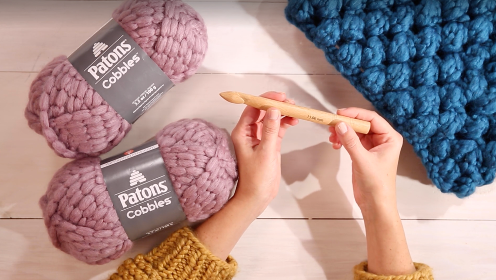 how to crotchet for beginners, woman holding a crotchet needle with yarn on the table