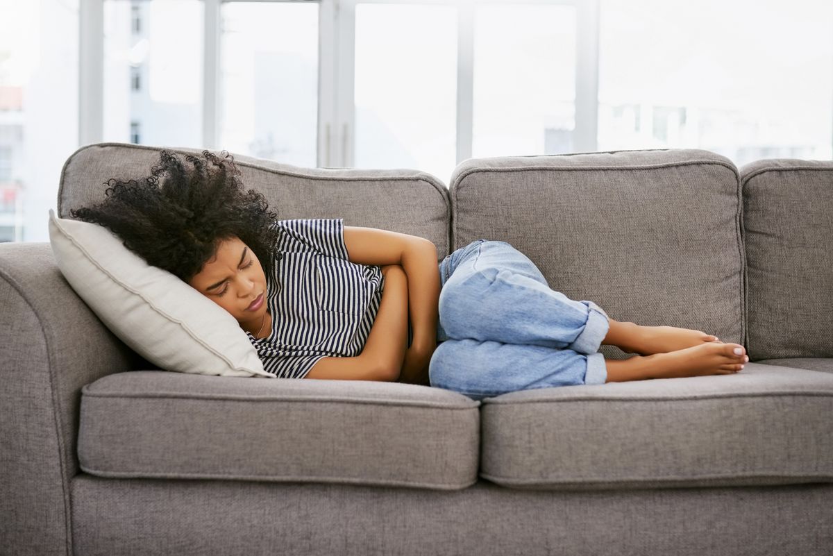 Woman lying on couch with arms wrapped around midsection.
