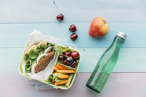 Lunch box with sandwich, cherries, carrots, and celery next to bottle of water.